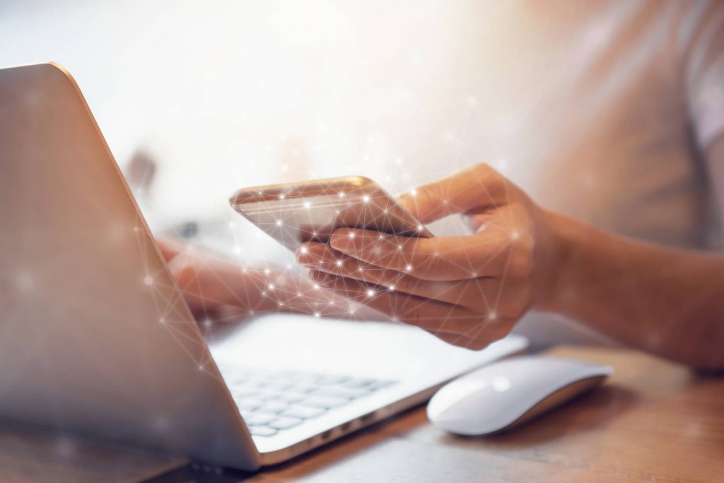 A woman at a computer holding her phone